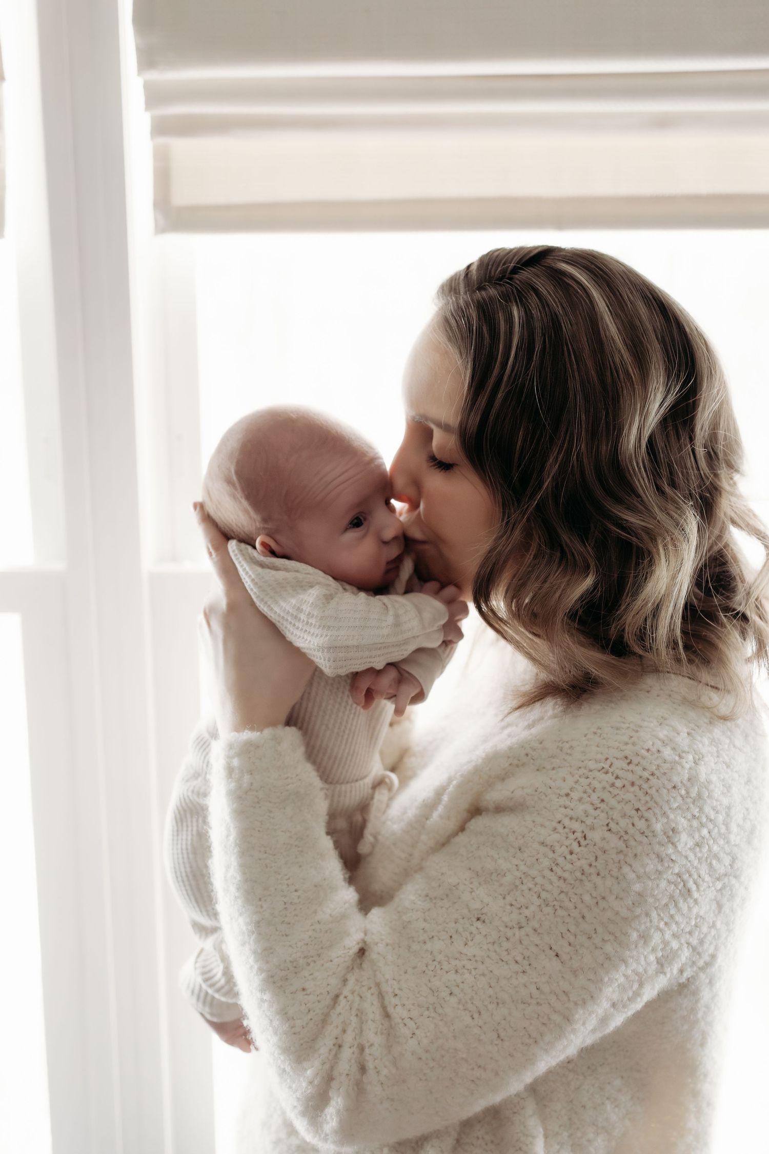 A tender moment between parent and newborn baby in a bright room with white window blinds.