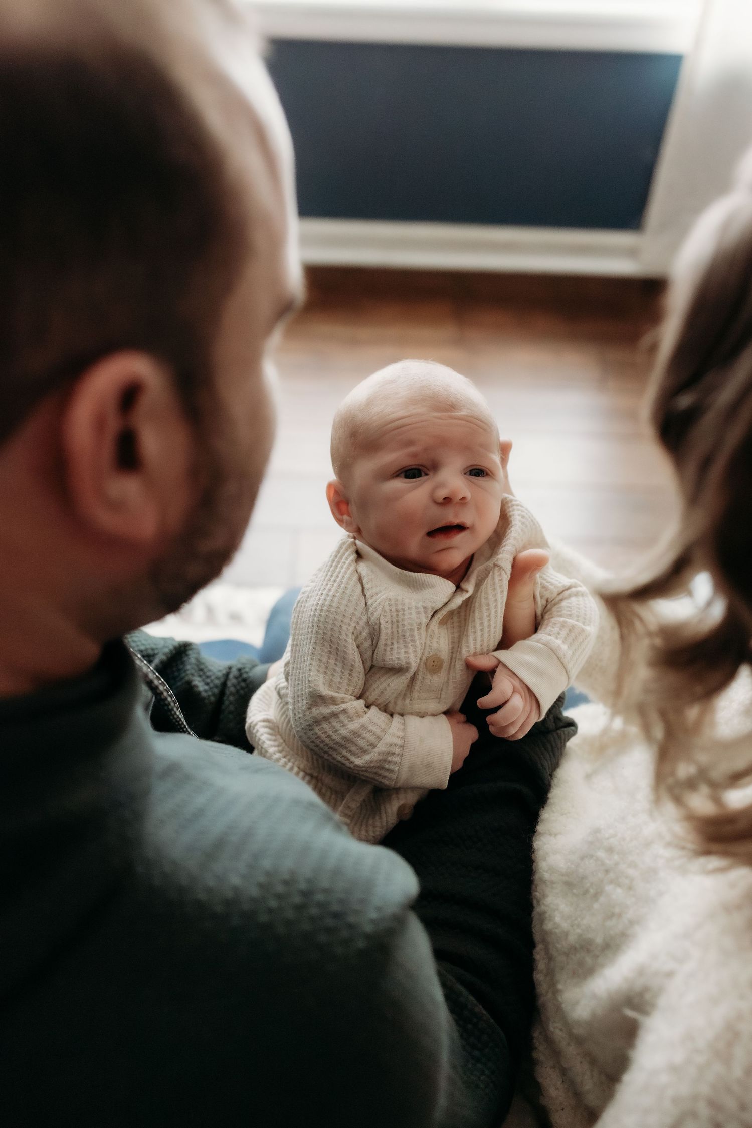 A baby in a cream sweater smiles while being held in a candid photo series.