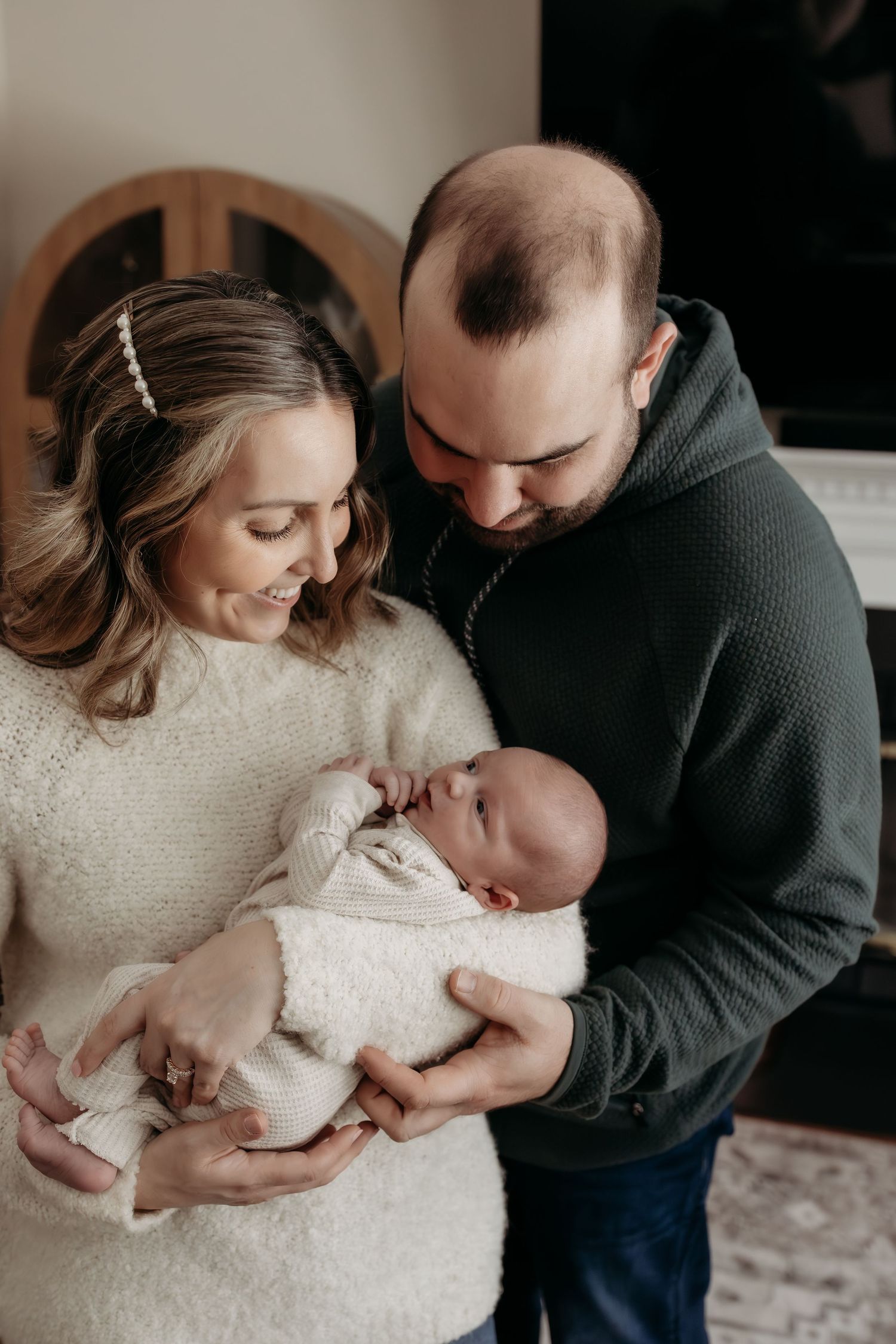 A couple in casual attire shares tender moments with their newborn baby in a series of intimate indoor portraits.