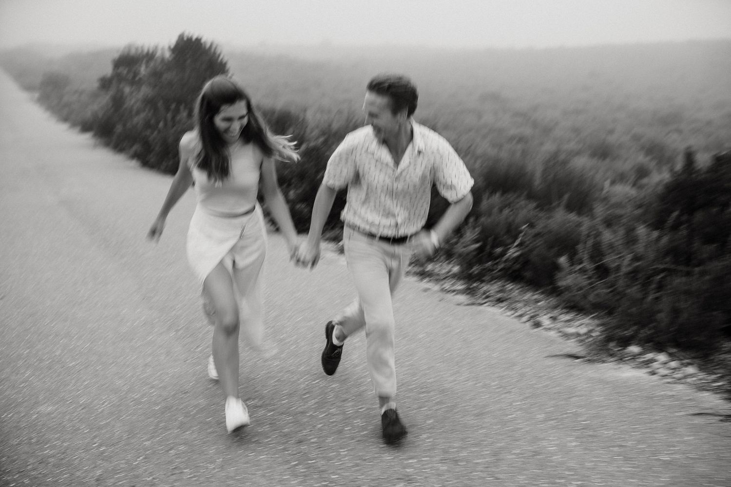 A couple runs playfully together on a hilltop path in this vintage black and white photograph.