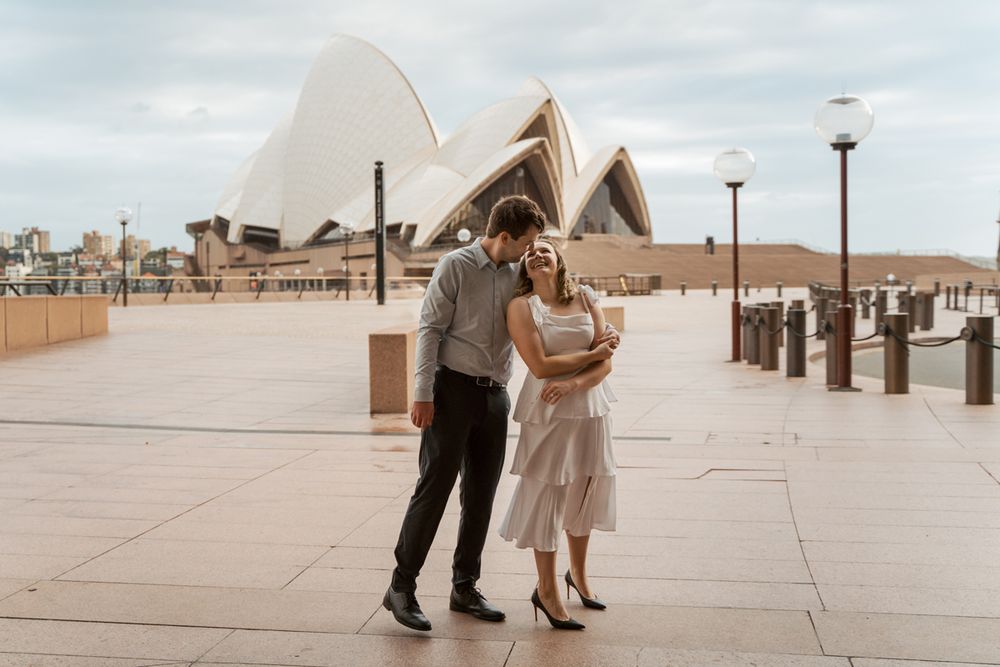 A couple dances on a boardwalk with the Sydney Opera House visible in the background during sunrise engagement photoshoot