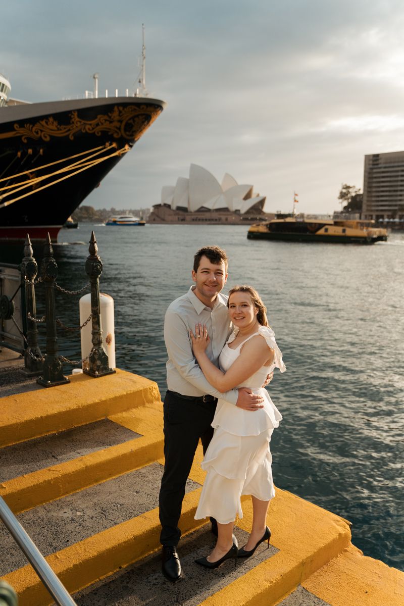 Couple poses for romantic sunrise photos at Sydney Harbour with Opera House and cruise ships in the background during an engagement session