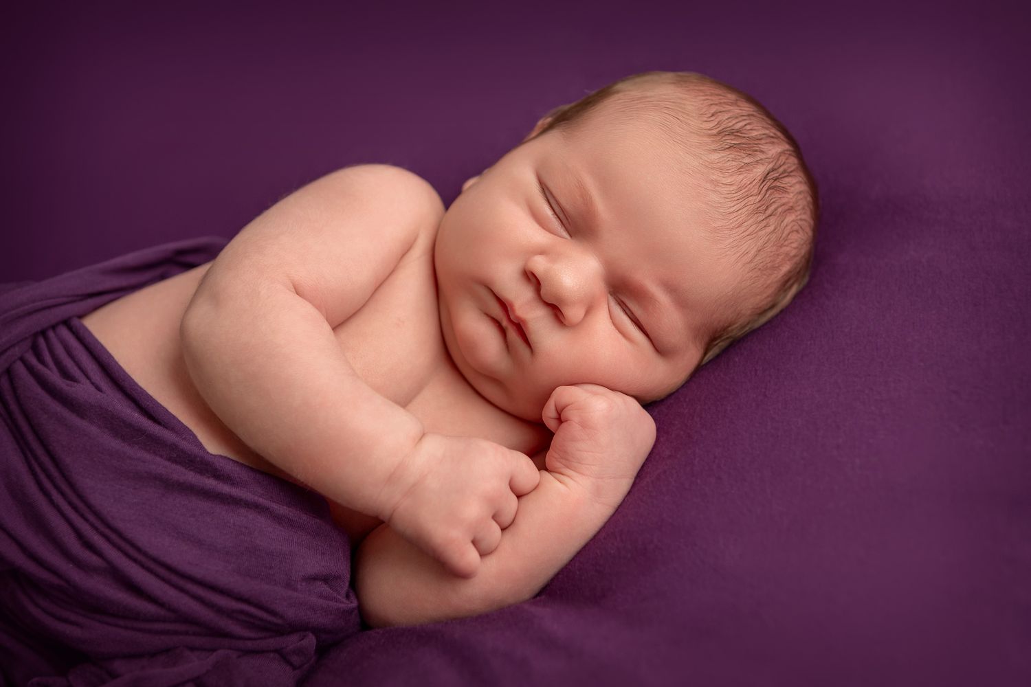 Newborn baby girl wrapped in dark purple