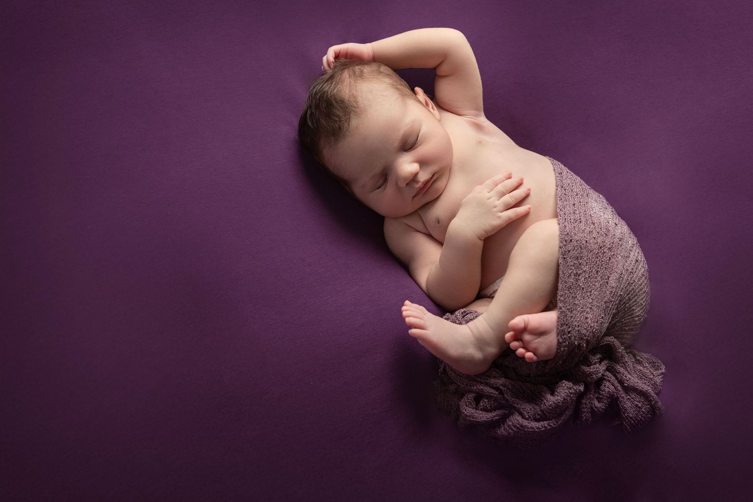Newborn baby sleeping peacefully in a dark purple wrap at a Warkworth photography studio