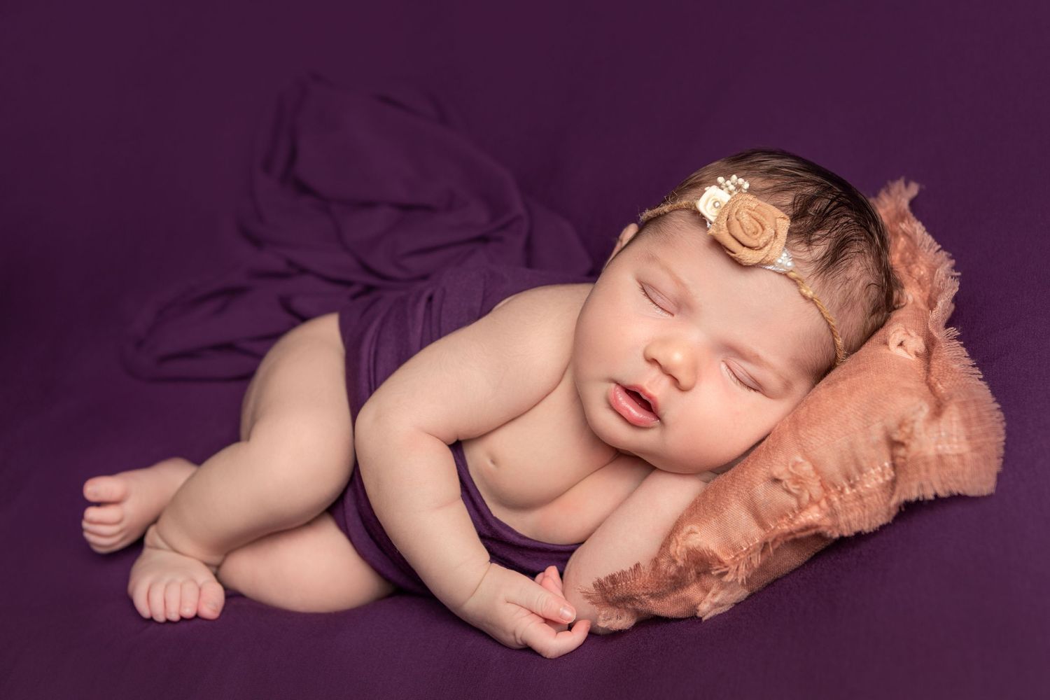Newborn baby sleeping peacefully in a dark purple wrap at a Warkworth photography studio