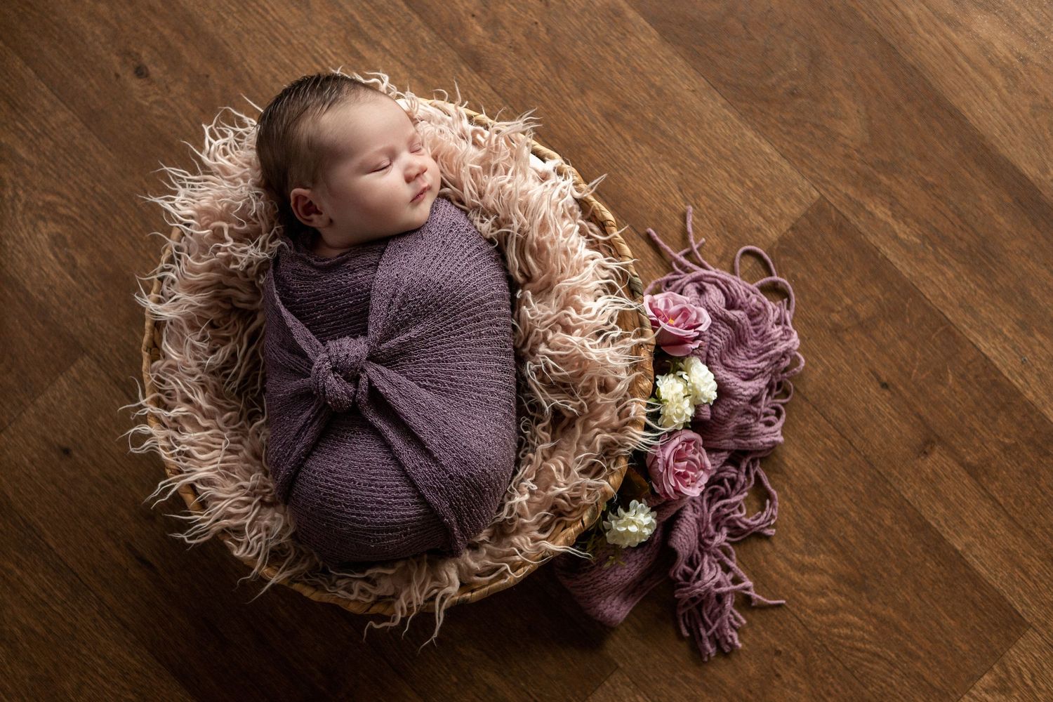 Baby girl wrapped in purple, sleeping in a basket