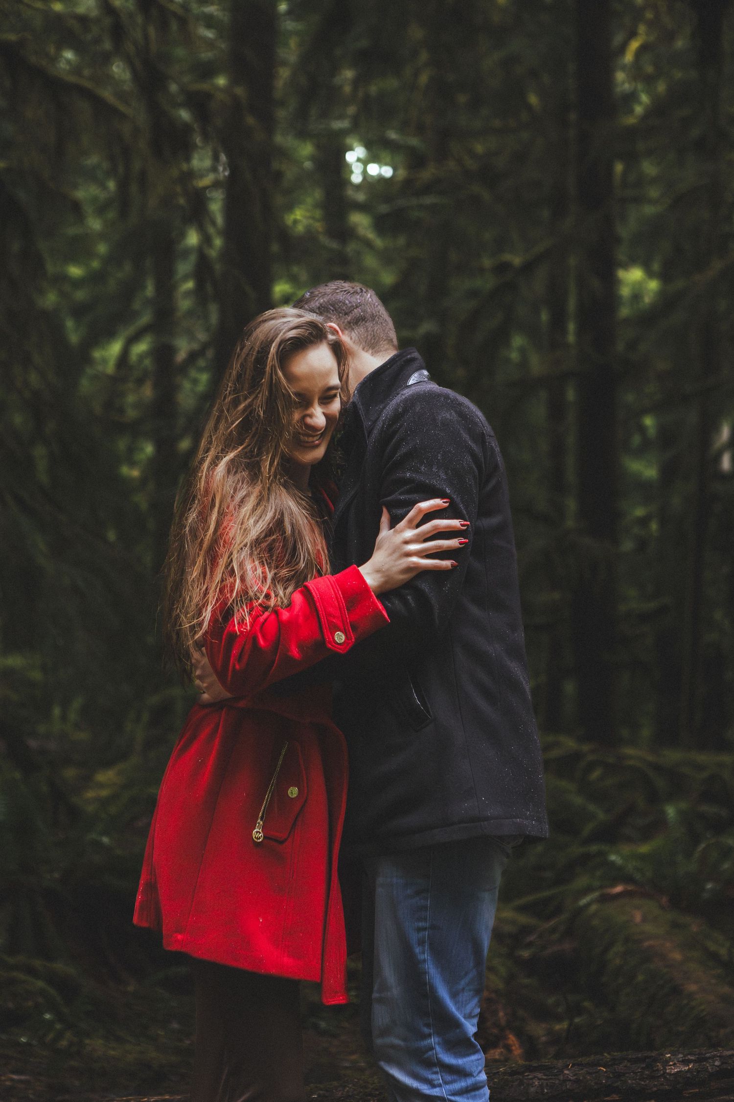 Couple in red and navy sharing intimate moment in evergreen forest.