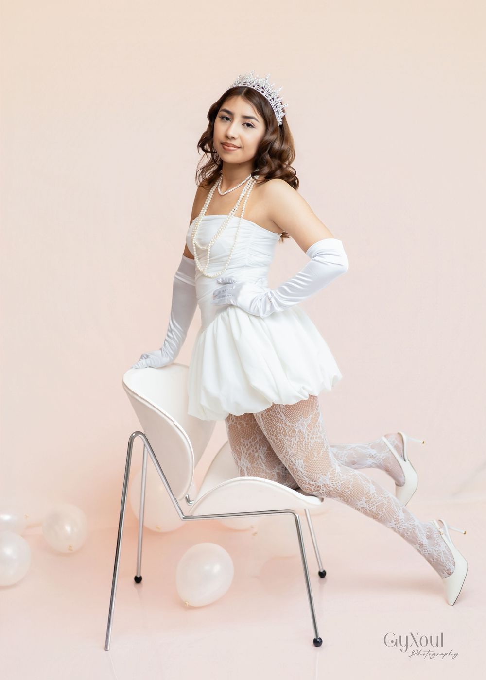 A figure in a white dress and gloves strikes elegant poses on a white chair against a pale pink background.