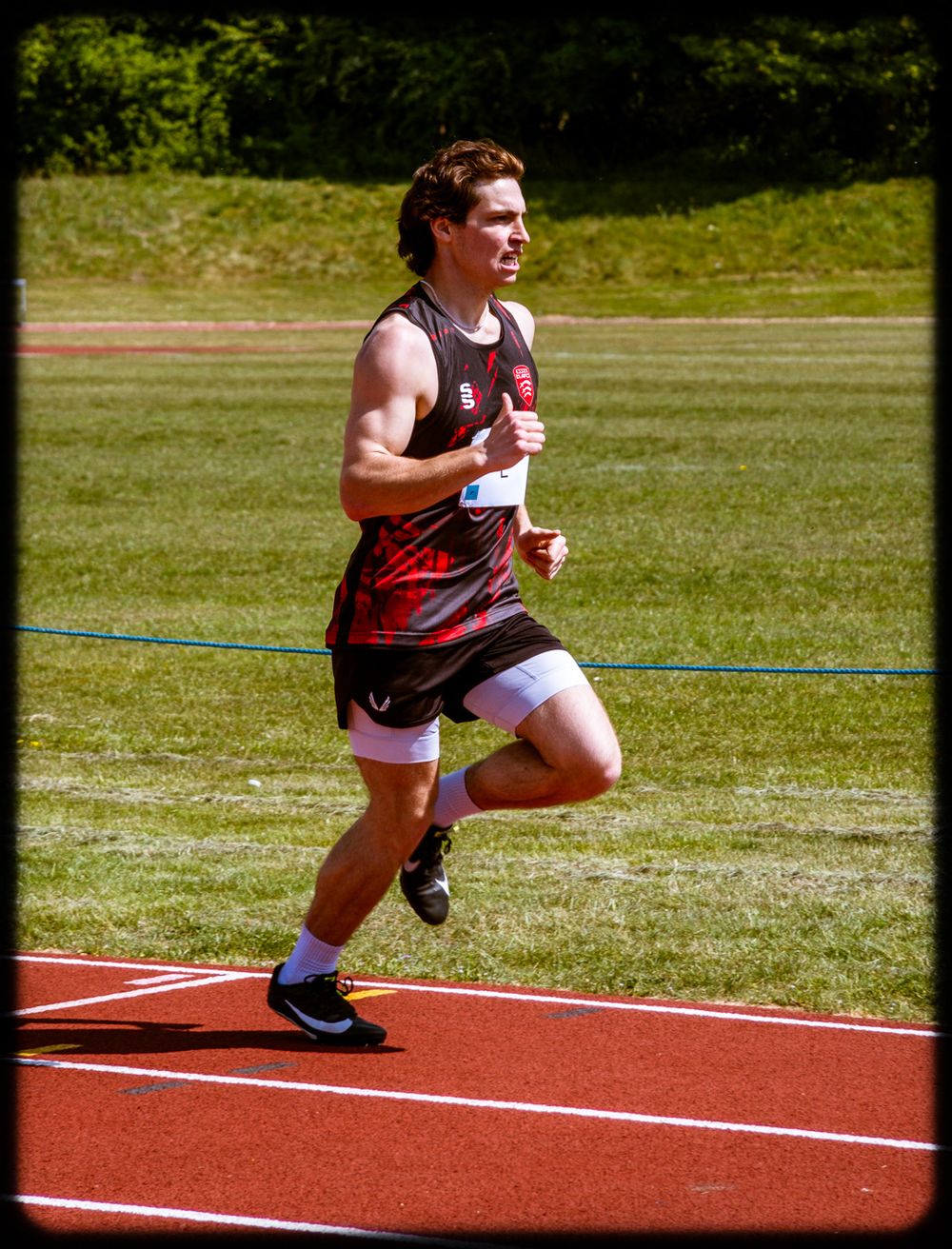 An athlete sprints on a red running track during an outdoor competition on a sunny day.
