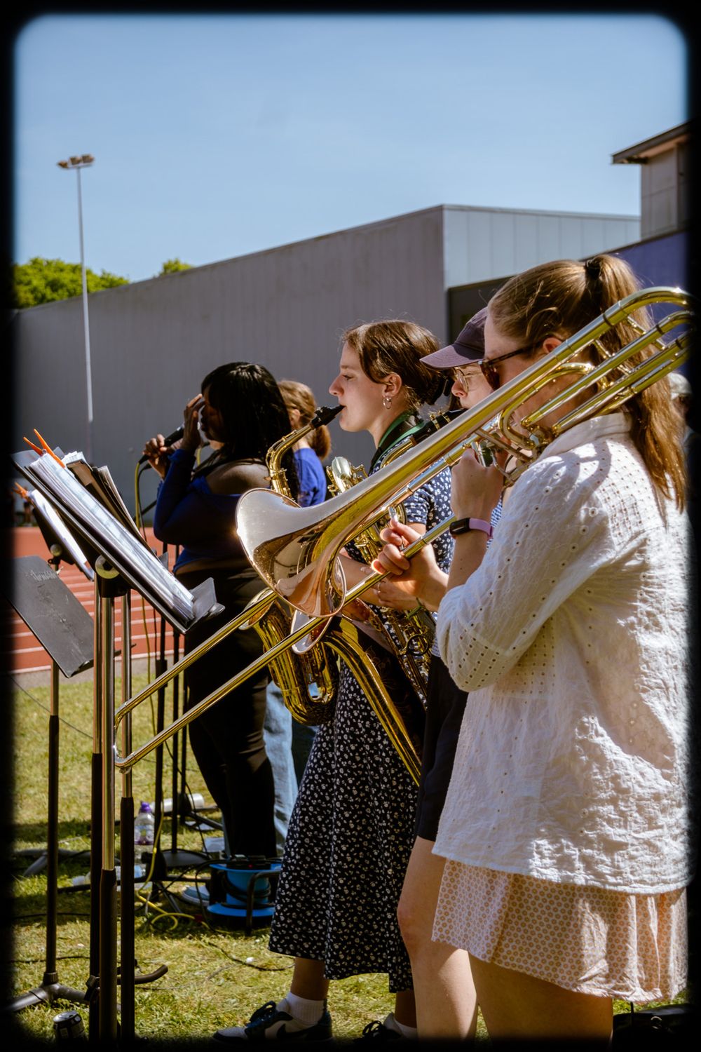 Musicians playing brass instruments outdoors in a line during a summer performance.
