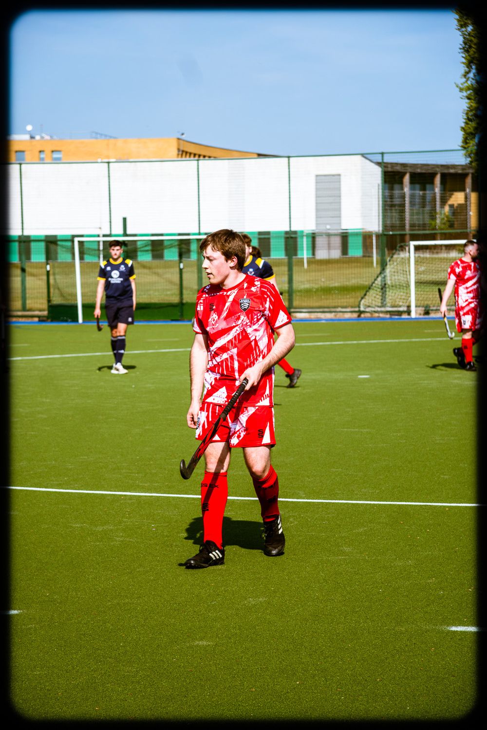 Soccer players in red uniforms compete on a green artificial turf field during a match.