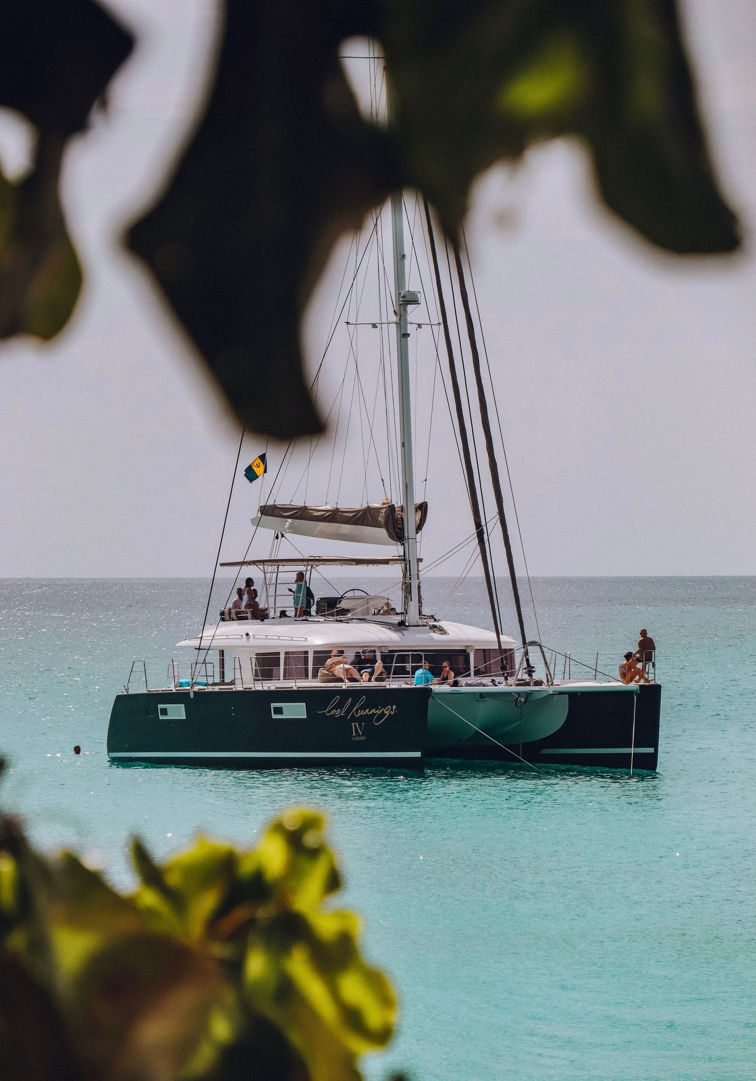A luxury catamaran sailboat anchored in crystal clear turquoise waters near a tropical shoreline.