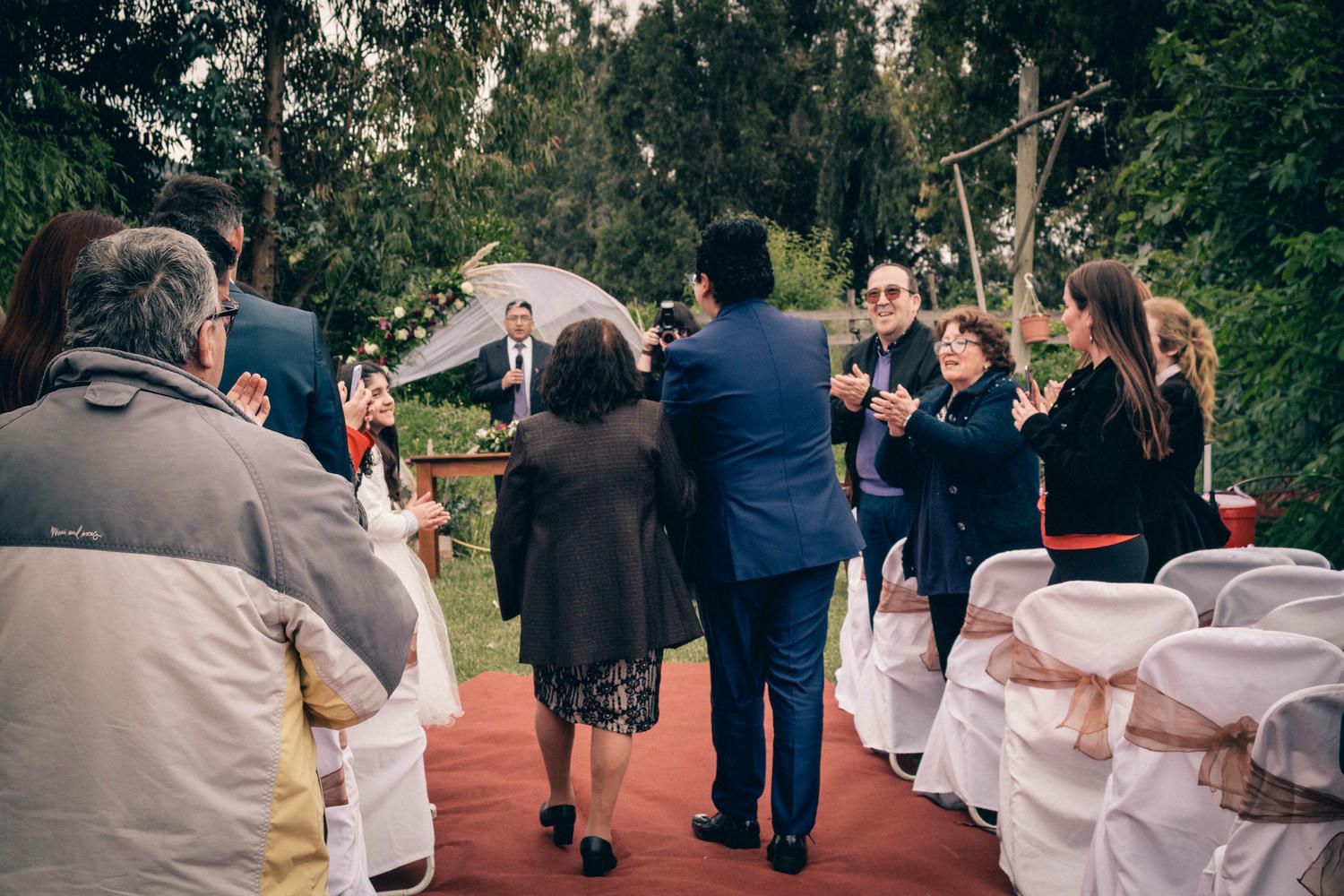 Invitados reunidos al aire libre bajo árboles otoñales durante celebración de matrimonio.