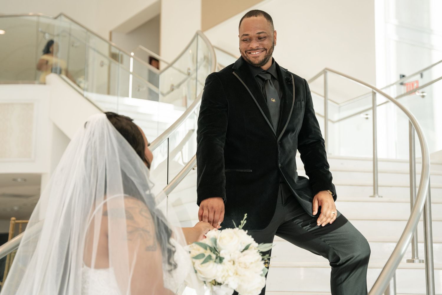 A bride and groom share a joyful moment on a modern white staircase during their wedding celebration.
