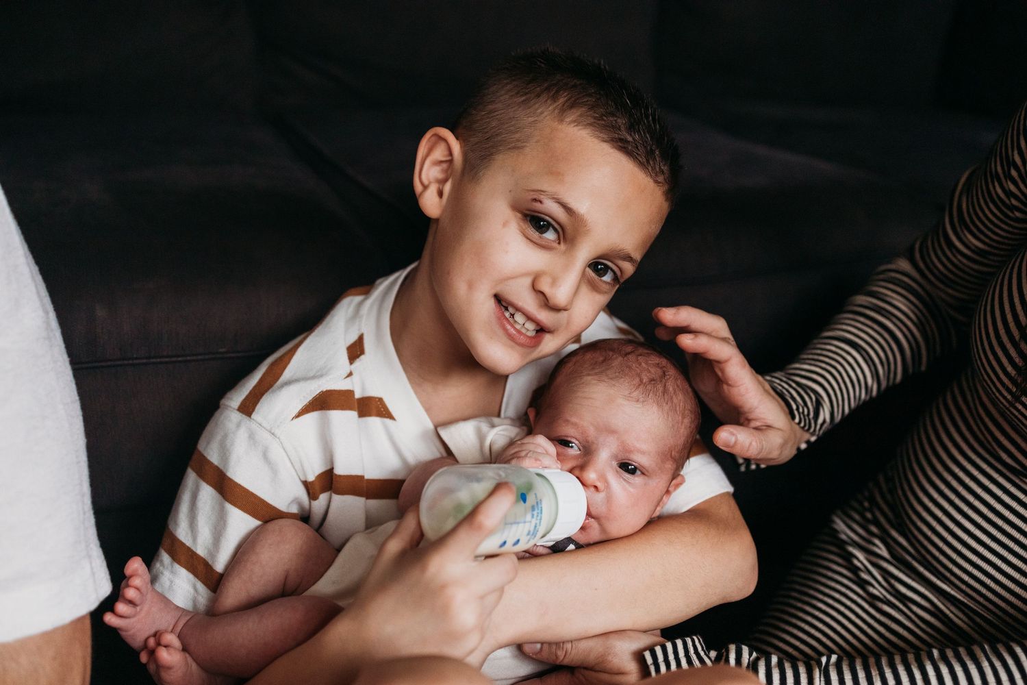 A parent tenderly cuddles with their infant child on a couch while wearing a striped shirt.