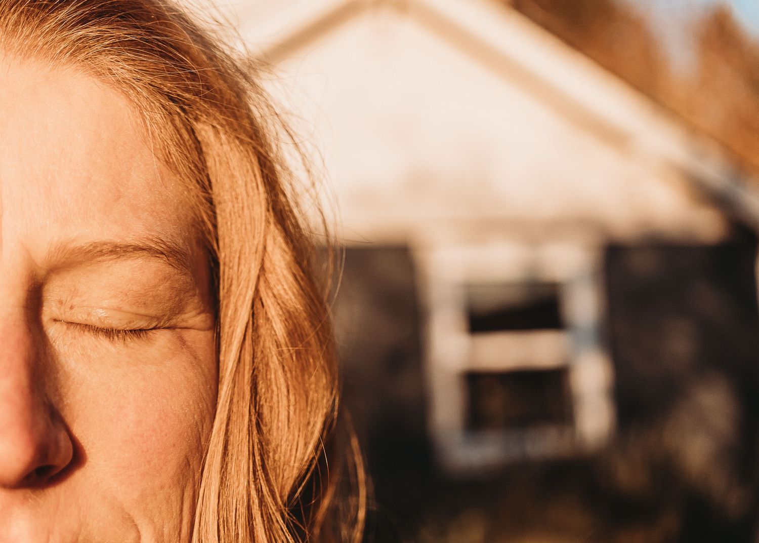 Close-up portrait showing closed eyes and blonde hair in warm sunlight against a blurred background.