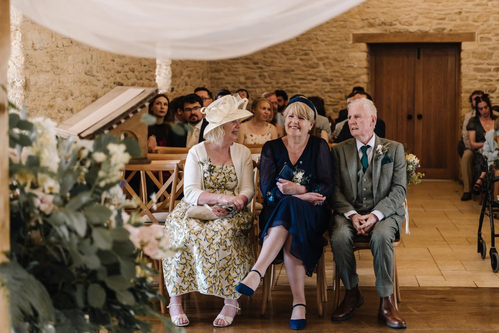Guests seated at a rustic barn wedding ceremony, including an elegant woman in a floral dress and hat.