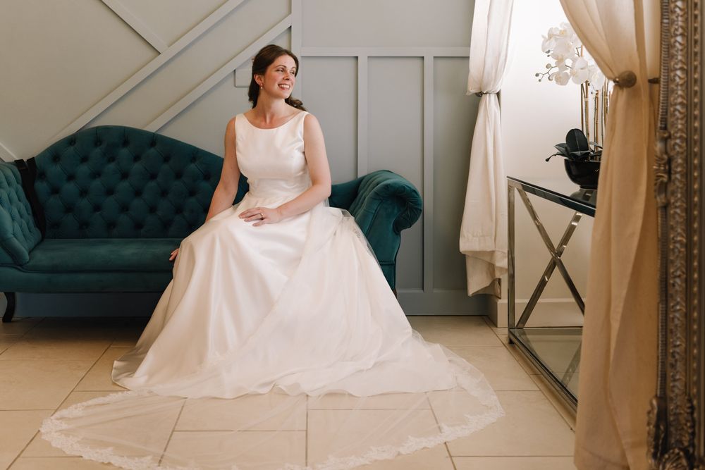 Bride in a white ball gown wedding dress sitting on a teal velvet sofa, smiling in an elegant room.