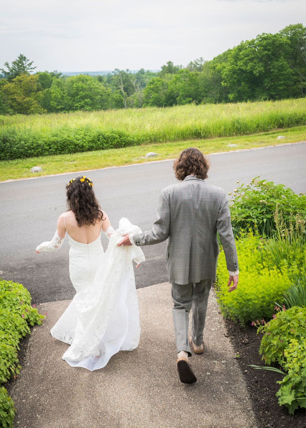 Bride and groom walking hand-in-hand down a garden path surrounded by lush greenery on their wedding day.