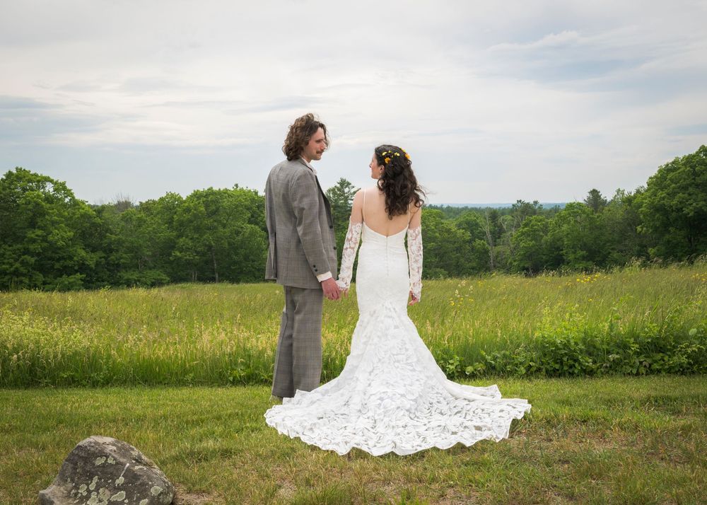 Bride and groom holding hands in a meadow, showcasing the stunning lace wedding dress train.