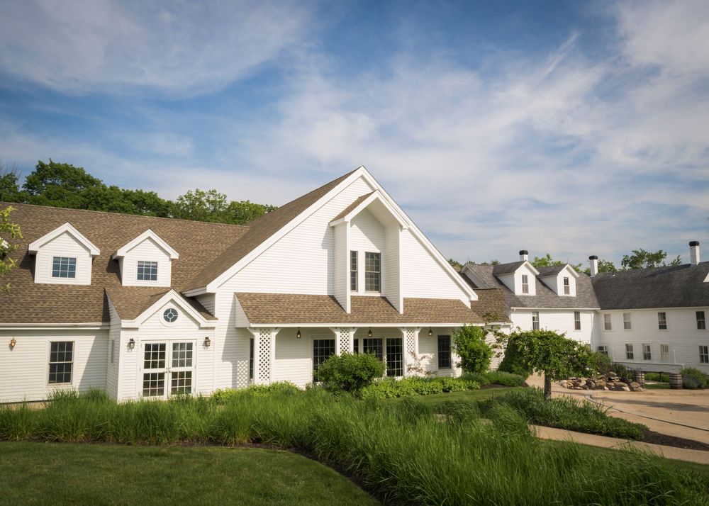 Elegant white New England wedding venue with manicured gardens under blue sky with scattered clouds.