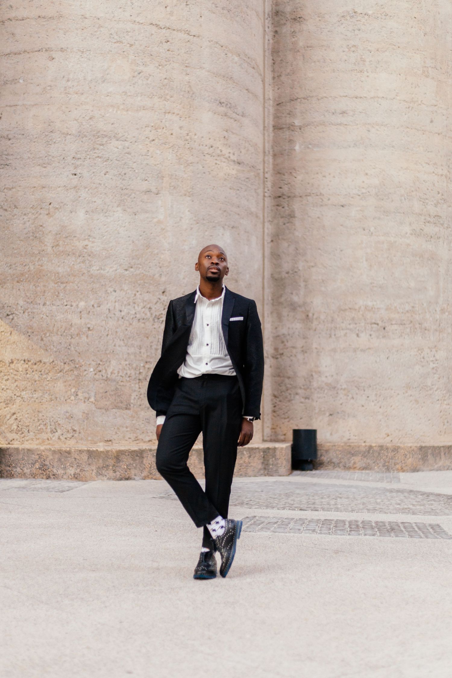 Person in business attire posing against stone columns in architectural setting.