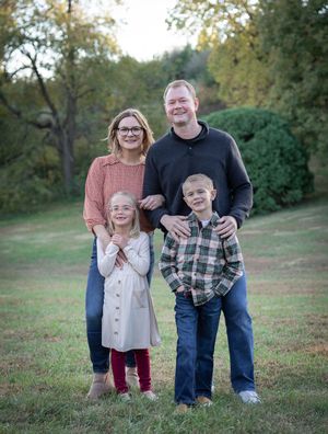 Family group portrait in a park with autumn trees in the background.