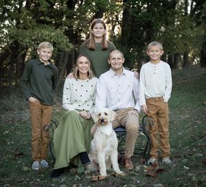 Family portrait with white dog sitting together on fallen log in wooded setting.