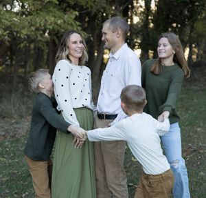 Candid family photo with children playing and laughing in outdoor forest setting.