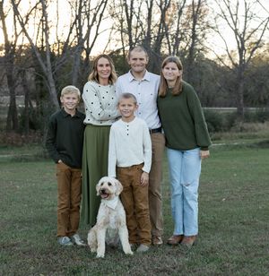 Wide family portrait with white dog in natural outdoor setting at dusk.