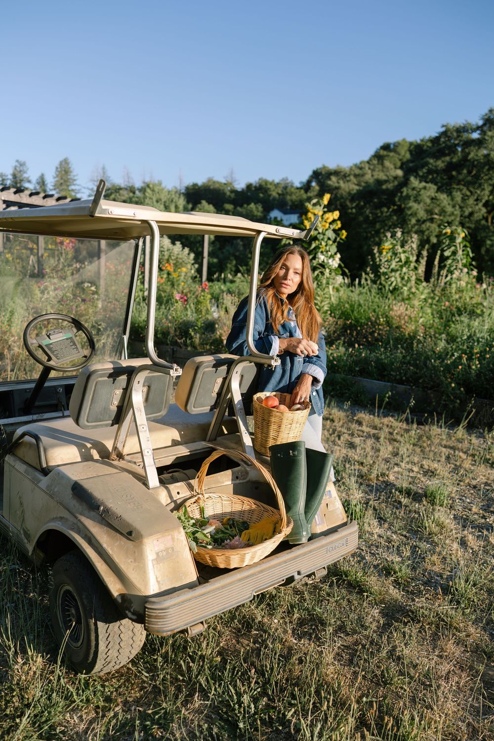 Golf cart with wicker basket parked in a sunny field with greenery.