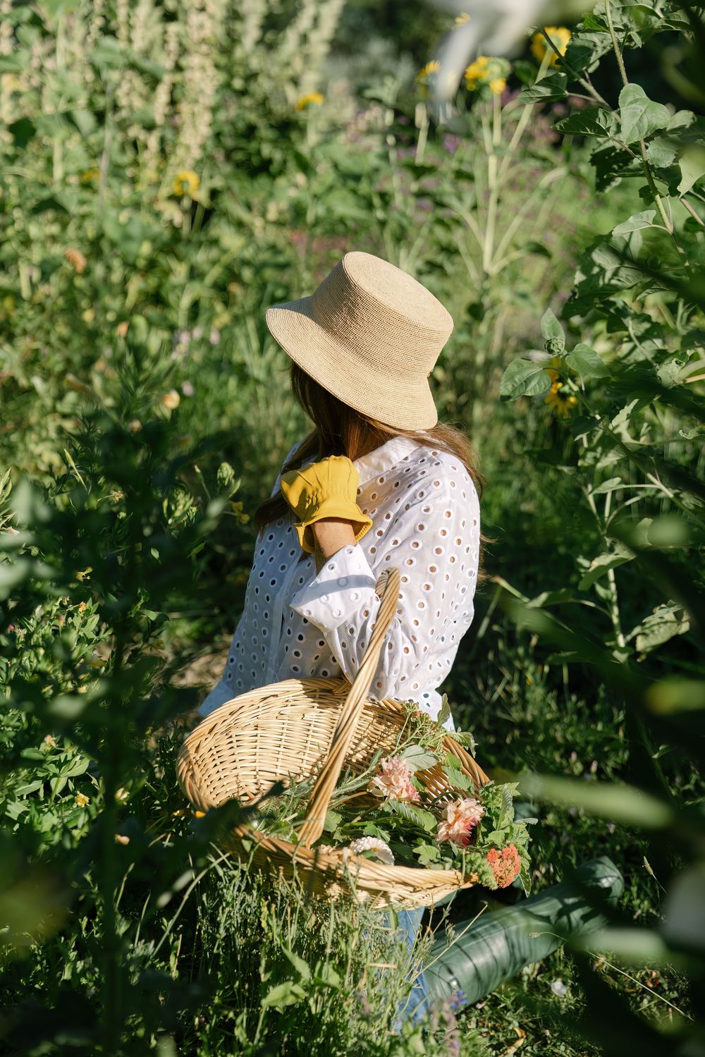 Garden harvest scene with figure in straw hat gathering flowers among green foliage.