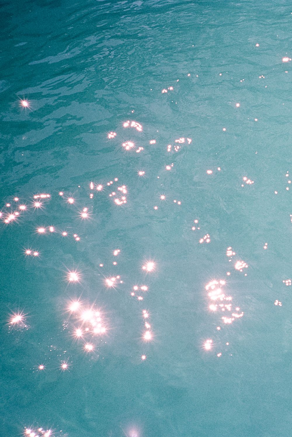 Sparkling sunlight reflections dancing across turquoise pool water surface.