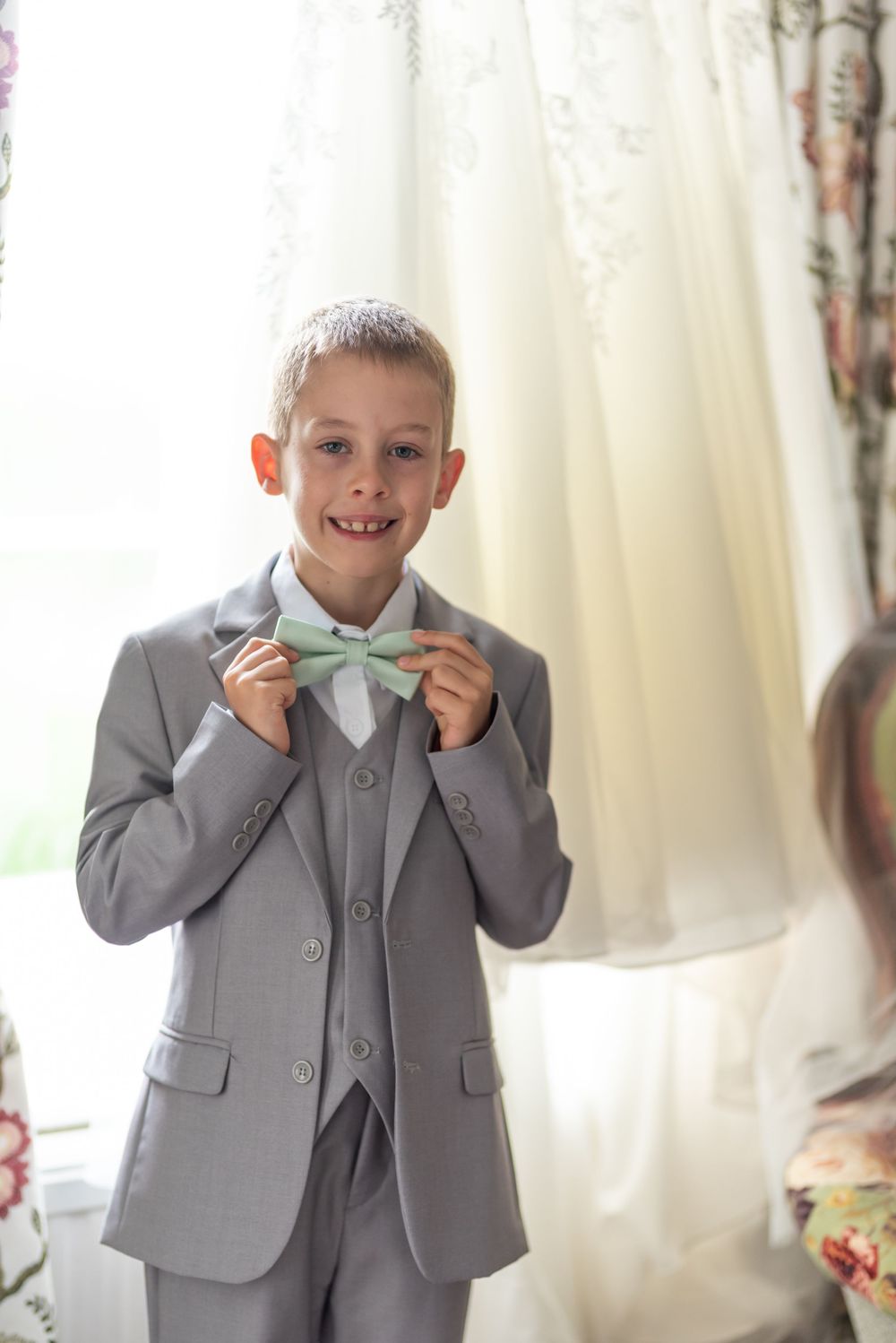 Young attendant in gray suit making playful expressions while adjusting bow tie.