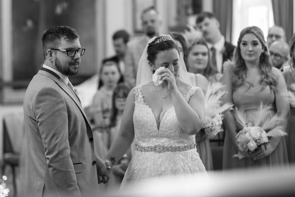 Wedding couple exchanging vows in front of gathered guests during indoor ceremony.