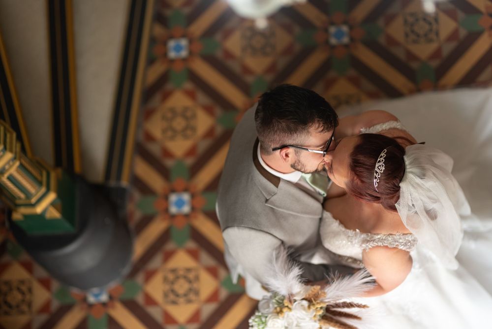 Intimate wedding moment captured under ornate ceiling with geometric patterns.