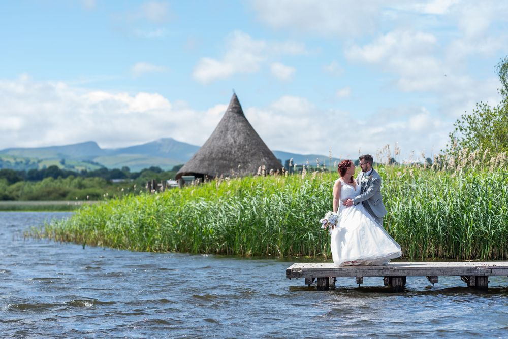 Wedding couple poses on rustic wooden dock surrounded by water and reeds.
