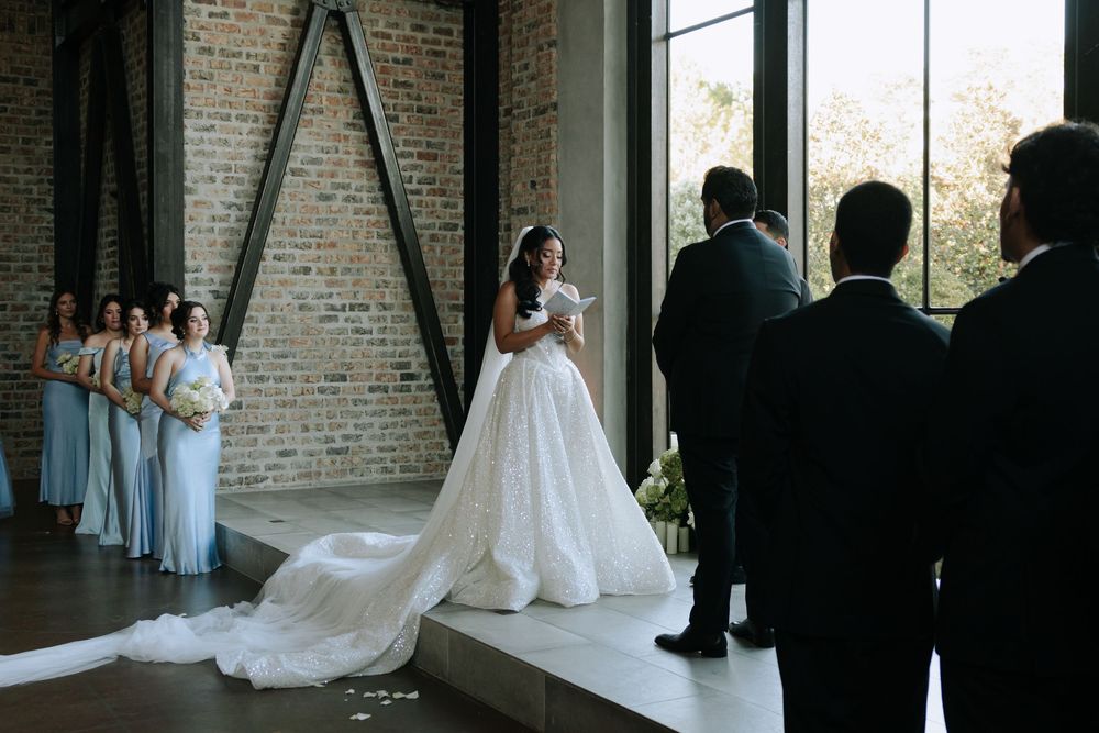 Wedding party gathers in elegant brick venue with large windows.