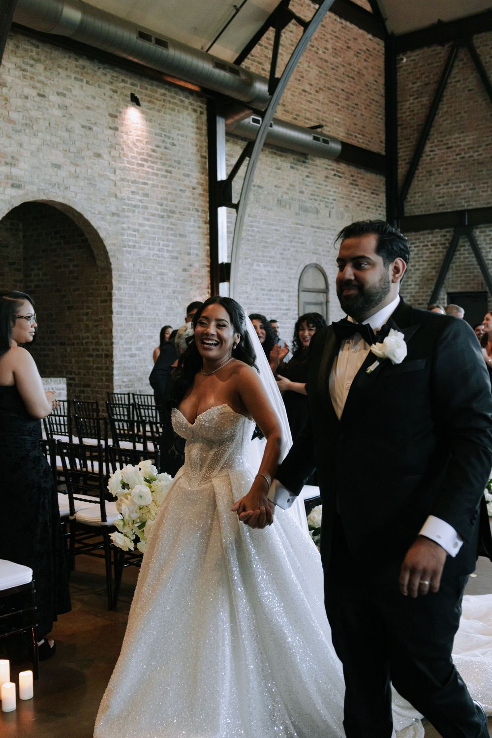 Wedding celebration in an elegant brick-walled venue with guests and decor.