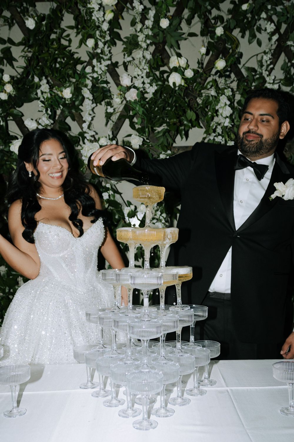 A couple pours champagne into an elegant tower of glasses at their wedding reception.