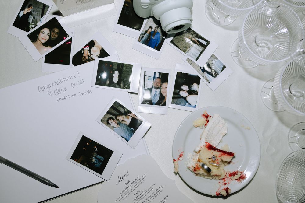 Wedding reception table settings with scattered polaroid photos and wine glasses on white tablecloths.