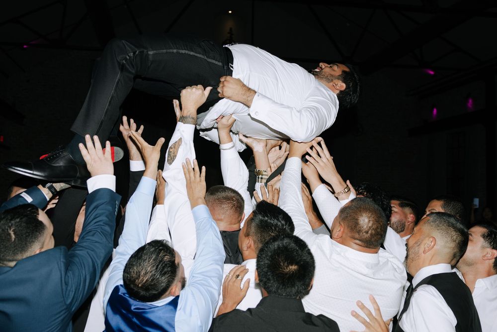 Crowd of people dancing with raised hands at a dark nightclub or party venue.