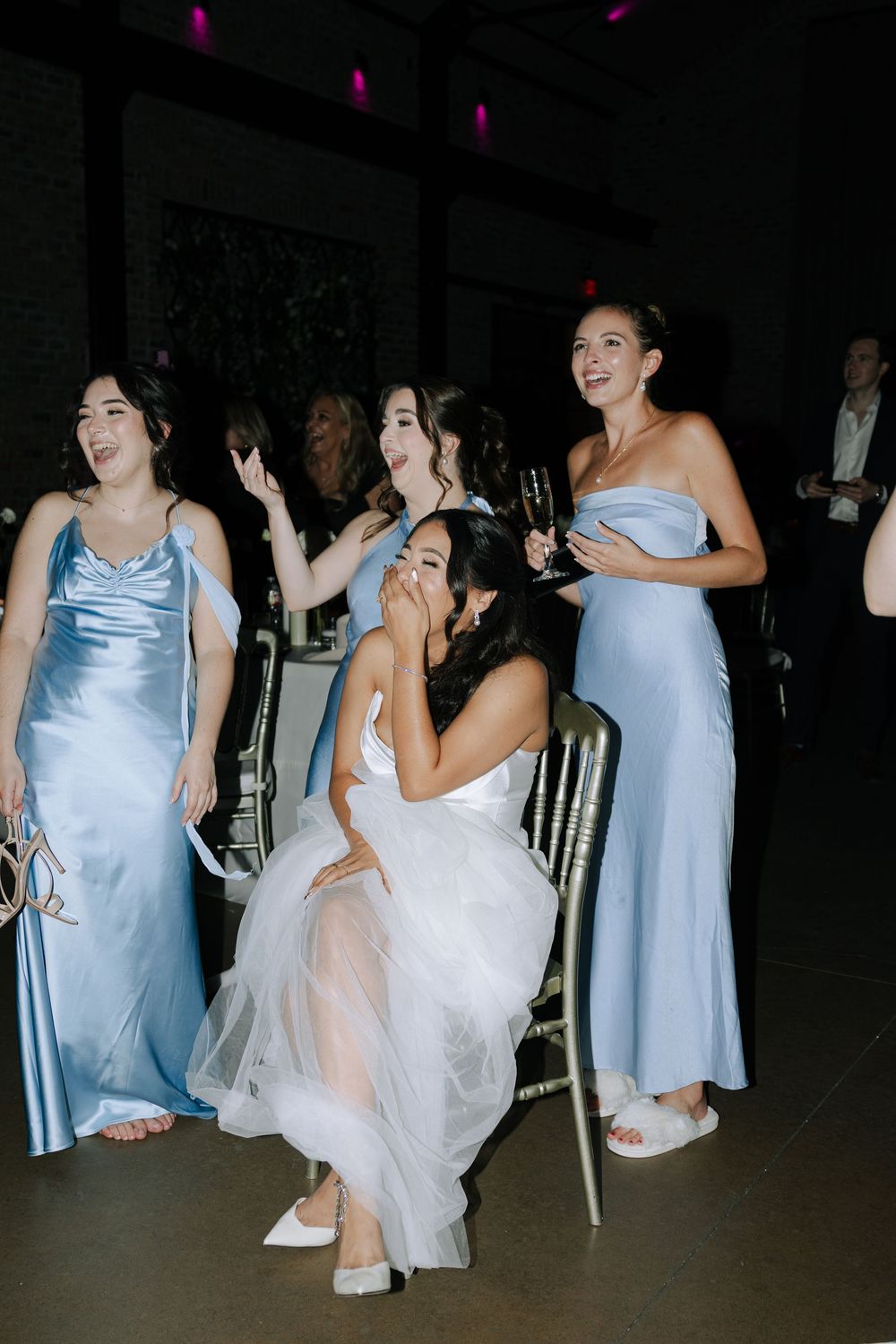 Bridesmaids in light blue dresses and wedding guests dancing together at a dimly lit reception.