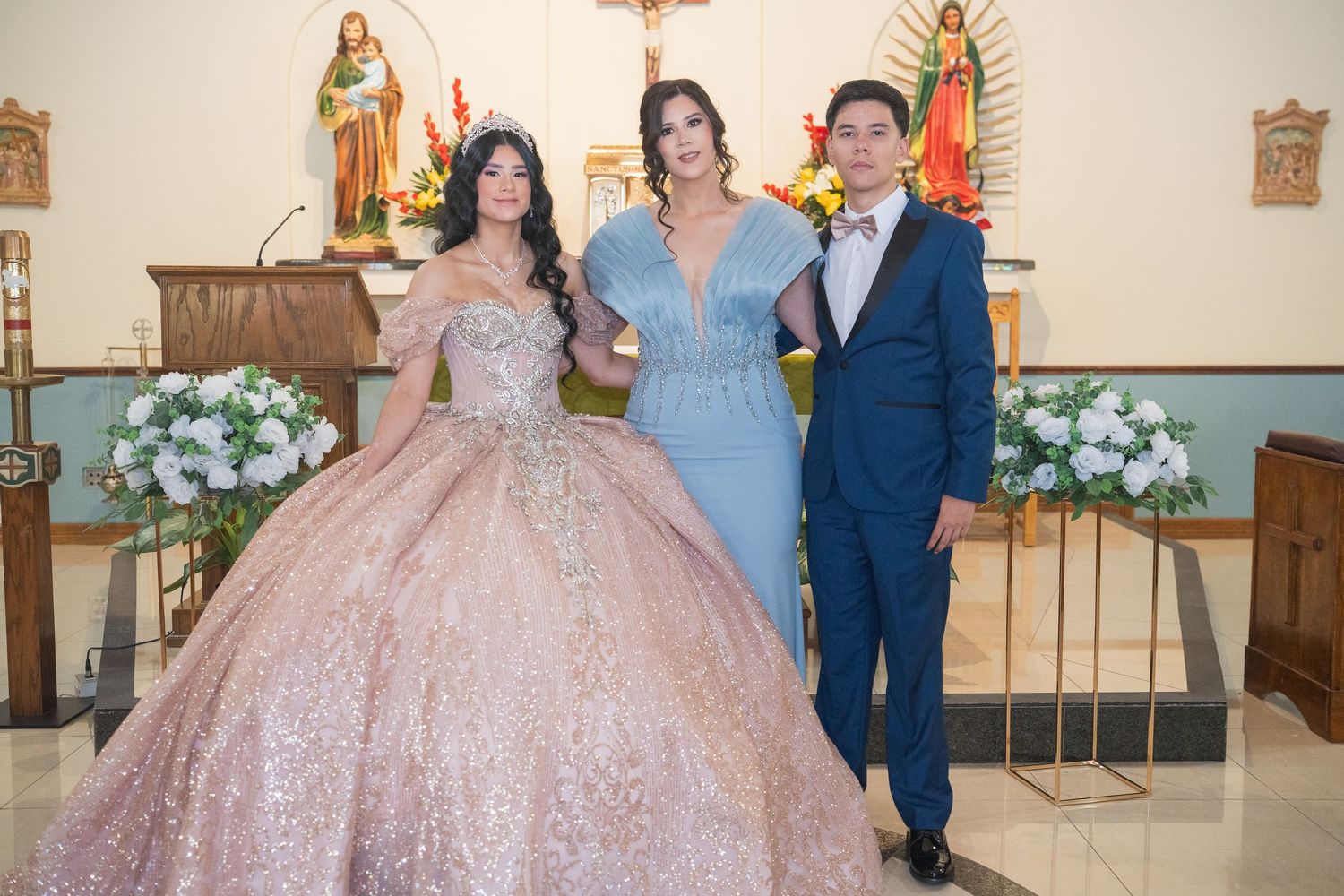 A quinceañera celebration in a church with religious icons and pink floral arrangements.