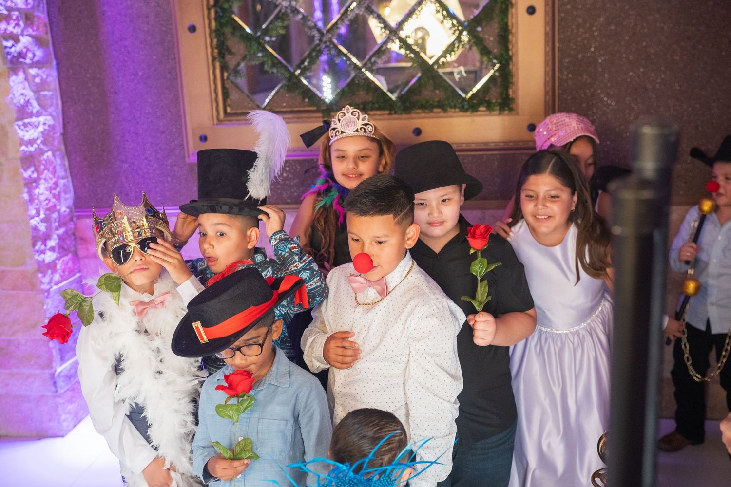 A group of children dressed in costumes pose together at a festive party with decorative lighting.