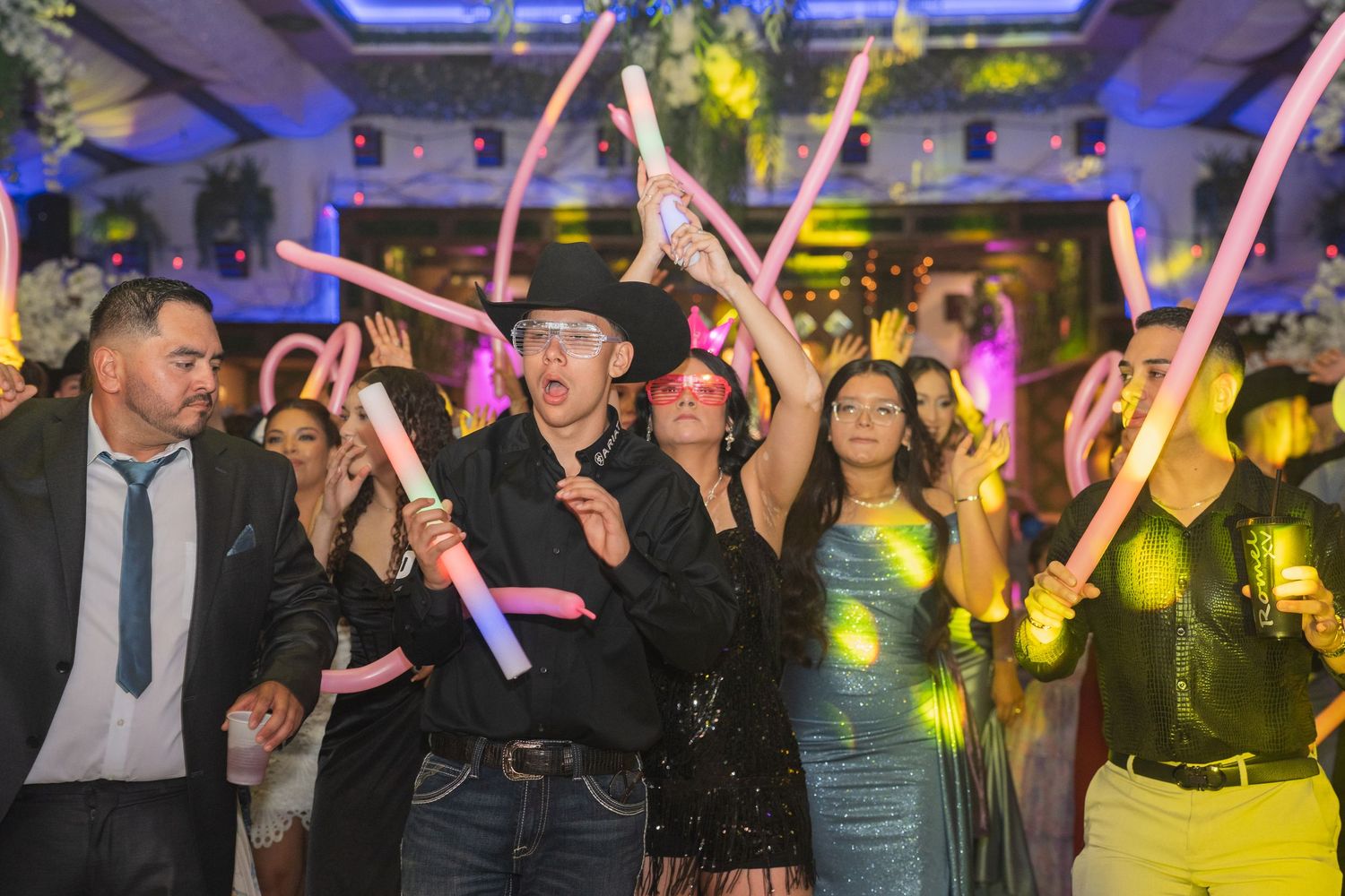 Energetic party crowd dancing with neon light sticks in a dimly lit venue.