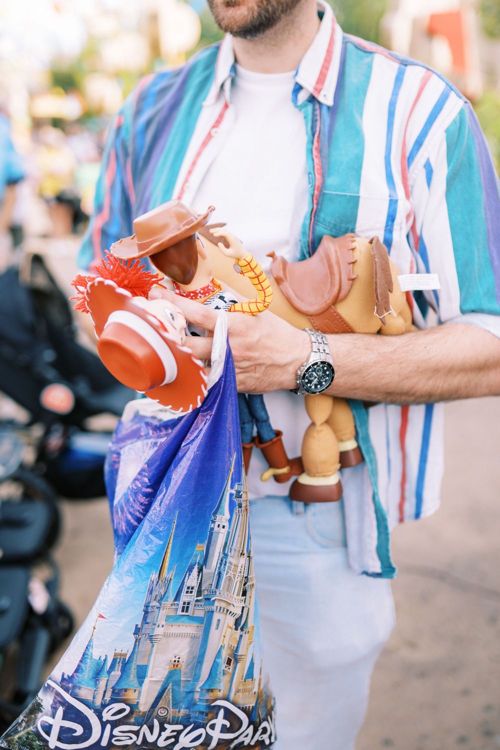 Person in striped shirt holds Disney World souvenir bag and Toy Story Woody doll merchandise at theme park.