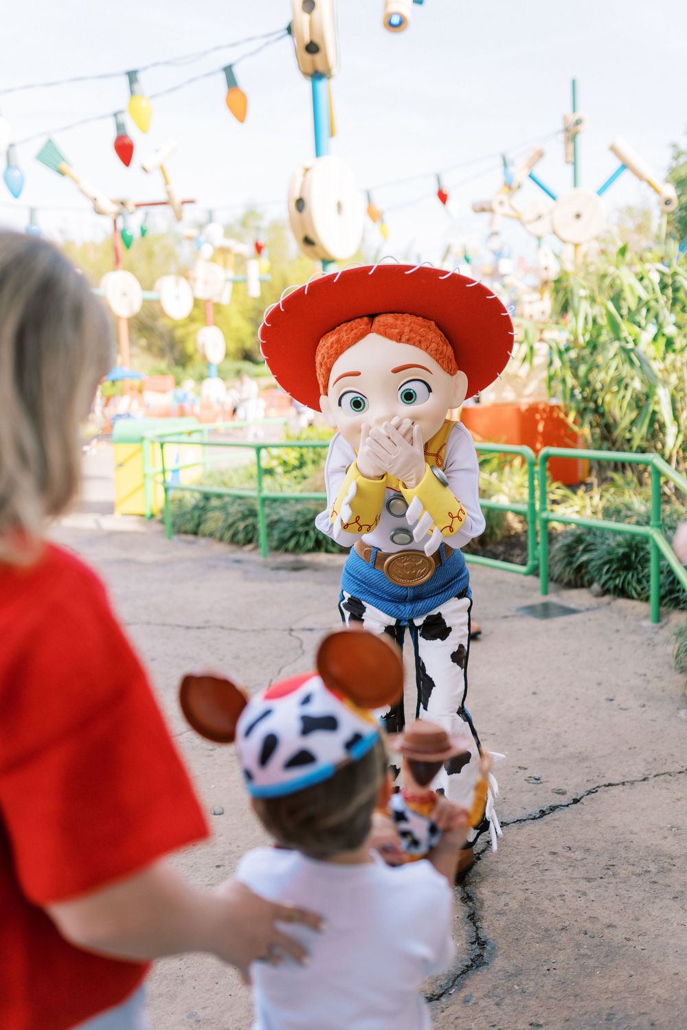 A Jessie character from Toy Story meets a small visitor in a theme park setting with colorful decorations.