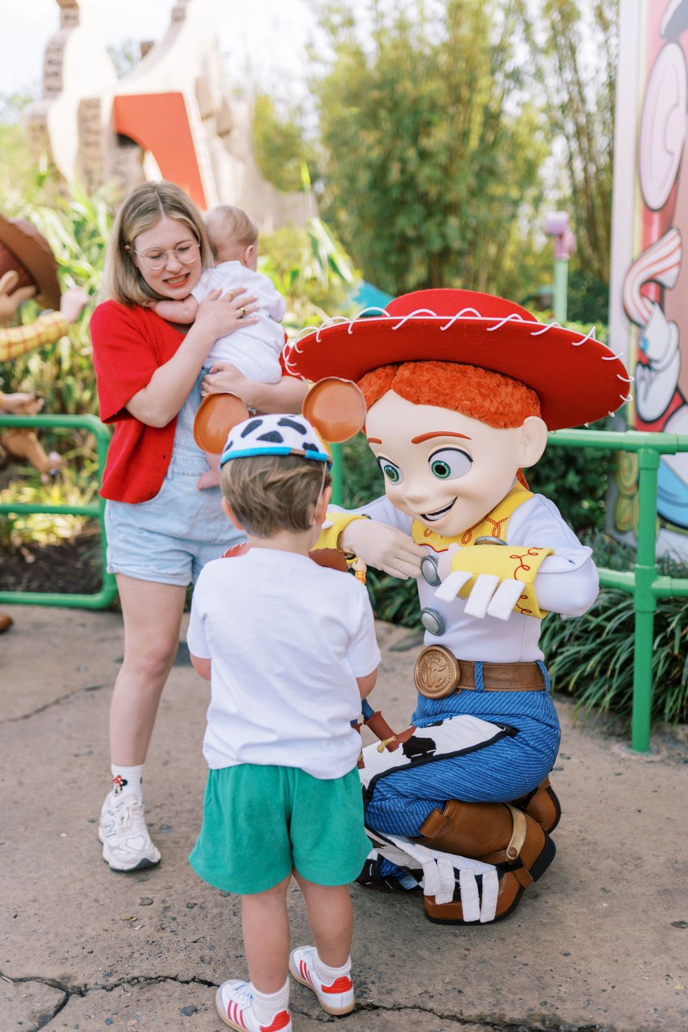A young child meets Jessie from Toy Story at a Disney theme park while another visitor looks on.