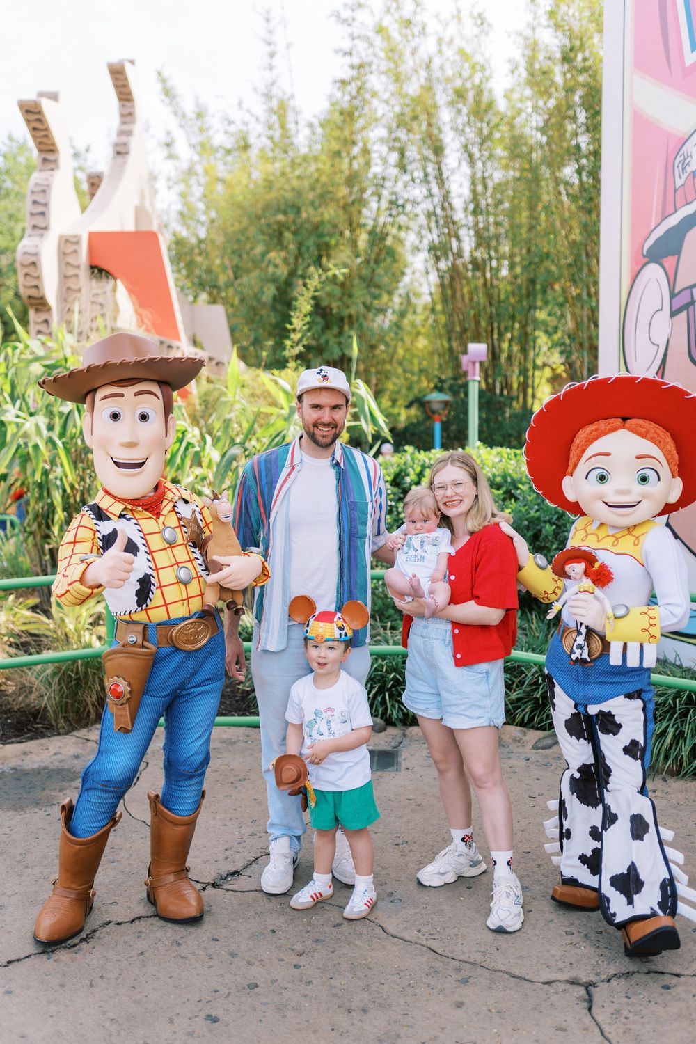 Toy Story themed characters pose with family visitors on a decorated pathway at a theme park.
